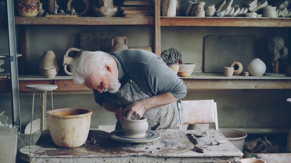 Senior man skillfully crafting a clay pot on a wheel in his pottery studio.